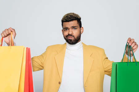 bearded african american man in yellow blazer and polo neck holding shopping bags isolated on greyの写真素材