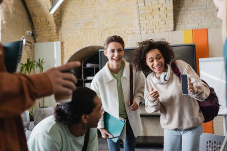 excited african american woman pointing at mobile phone near interracial classmatesの写真素材