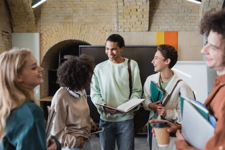 smiling african american student holding empty notebook near multiethnic friendsの写真素材