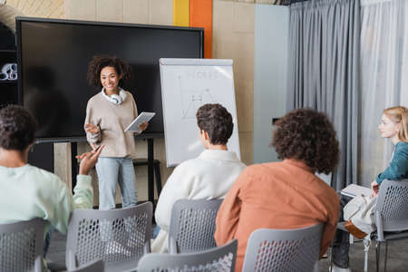 african american woman with digital tablet near whiteboard with task and interracial students in classroomの写真素材