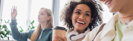 happy african american woman with coffee and headphones looking at blurred friend, bannerの写真素材