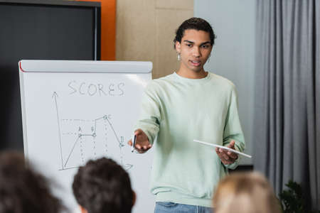 african american student with digital tablet pointing at blurred classmates near whiteboard with taskの写真素材