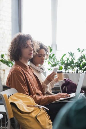 curly man using laptop near african american woman with coffee to go and mobile phoneの写真素材