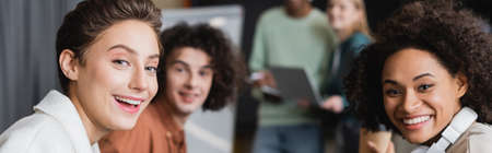 cheerful multicultural students looking at camera on blurred background, bannerの写真素材