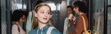 amazed woman looking away near interracial classmates on blurred background, bannerの写真素材