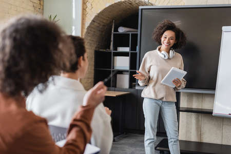 smiling african american student with digital tablet pointing at classmate on blurred foregroundの写真素材