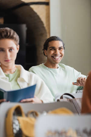 young african american man smiling during lecture in university near blurred classmateの写真素材