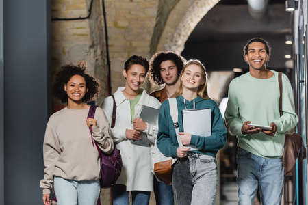 group of happy multiethnic students with backpacks and gadgets in universityの写真素材