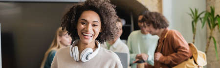 laughing woman with headphones looking at camera near classmates on blurred background, bannerの写真素材