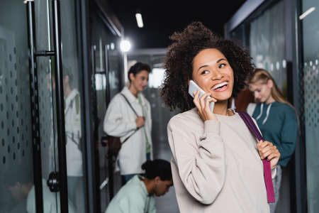 cheerful african american woman talking on cellphone near classmates on blurred backgroundの写真素材