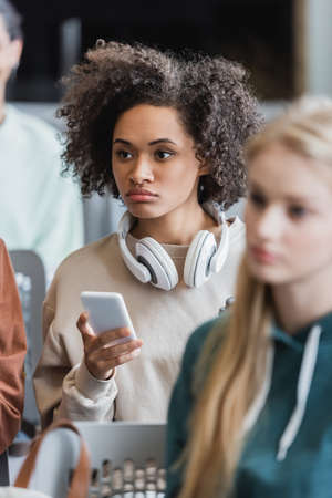 young african american woman with headphones holding smartphone during lecture near blurred studentsの写真素材