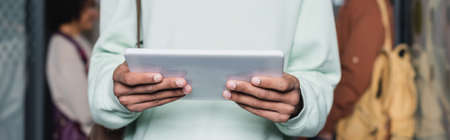 partial view of african american student holding digital tablet on blurred background, bannerの写真素材