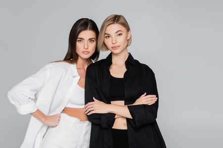 women in black and white shirts standing with hand on hip and crossed arms isolated on grey