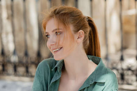 portrait of happy young woman with red hair and green linen shirt smiling outsideの写真素材