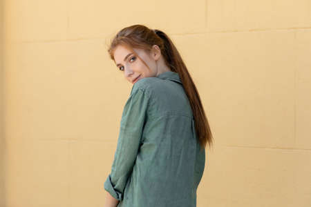 young woman in green linen shirt posing near beige wall on street
