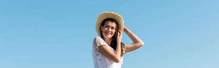 Low angle view of pretty woman in sun hat smiling at camera with blue sky at background, bannerの写真素材