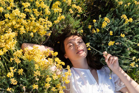 Top view of young woman lying on lawn with yellow flowers