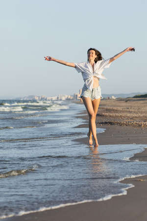 Happy woman in shorts and shirt walking near sea on beachの写真素材