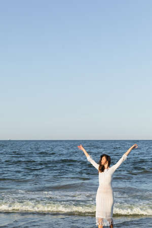 Positive woman in dress standing near sea with blue sky at backgroundの写真素材