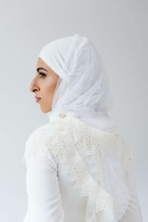 side view of muslim bride in hijab and white dress isolated on greyの写真素材