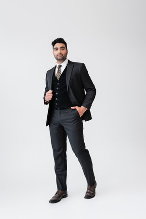 full length of muslim man in formal wear standing with hand in pocket on greyの写真素材