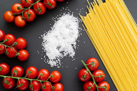 Top view of salt near uncooked spaghetti and cherry tomatoes on black backgroundの写真素材