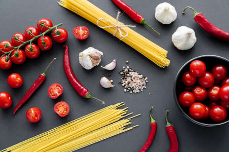 Top view of natural vegetables near spices and uncooked pasta on black surface