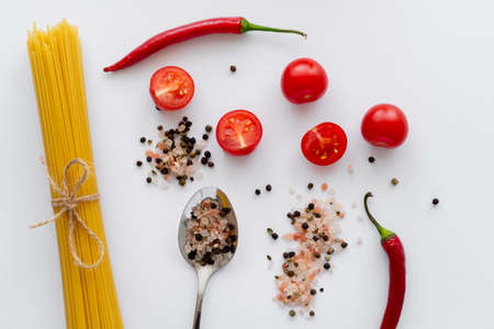 Top view of raw pasta near spices with cherry tomatoes and chili pepper on white background