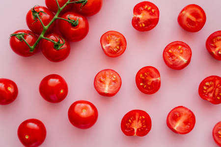 Top view of cut and whole cherry tomatoes on branch on pink background