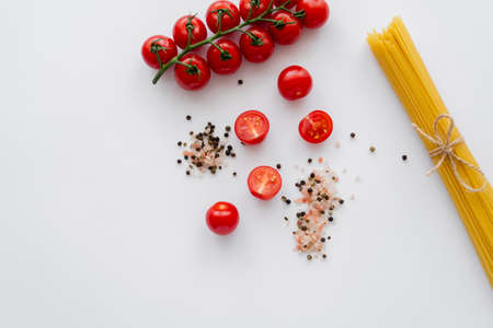 Top view of raw cherry tomatoes near spices and macaroni on white backgroundの写真素材