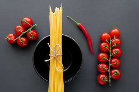 Top view of raw spaghetti on bowl near fresh vegetables on black surface