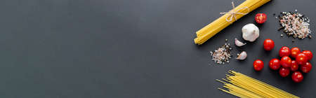 Top view of raw spaghetti near garlic and spices on black surface with copy space, bannerの写真素材