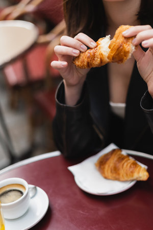 cropped view of woman holding croissant near cup of coffee in outdoor cafe in parisの写真素材