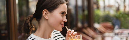 side view of smiling young woman holding glass of fresh orange juice in outdoor cafe in paris, bannerの写真素材
