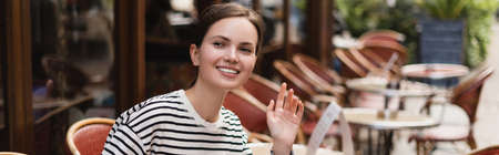 smiling woman in striped shirt waving hand in outdoor cafe in paris, bannerの写真素材