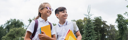 Multiethnic schoolchildren holding notebooks while looking away outdoors, banner