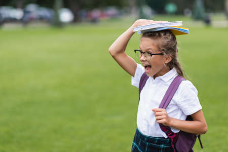 Excited schoolkid with backpack holding copy books on head outdoorsの写真素材