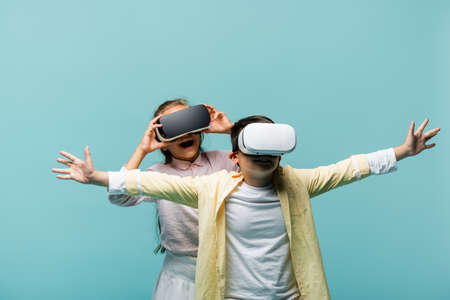 Positive preteen kids in vr headsets playing video game isolated on blue