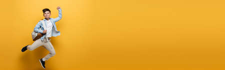 Asian kid with backpack showing yes gesture and jumping on yellow background, bannerの写真素材