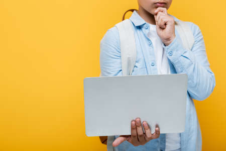 Cropped view of schoolkid holding laptop isolated on yellowの写真素材