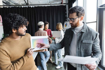 man in eyeglasses pointing at color samples near indian designer in ad agencyの写真素材