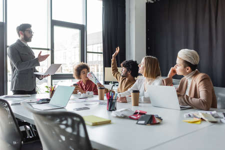 indian man with color samples raising hand during meeting with multiethnic team in ad agencyの写真素材