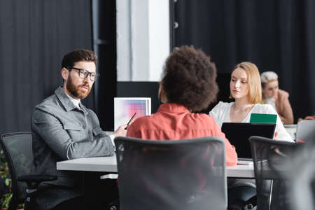bearded man in eyeglasses pointing at color samples near interracial advertising designersの写真素材