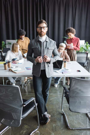 bearded businessman in eyeglasses looking at camera near multiethnic colleagues in advertising agencyの写真素材