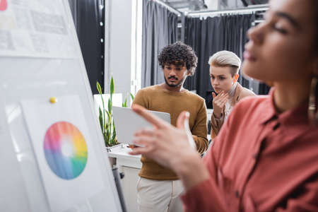 blurred african american woman pointing at flip chart near thoughtful interracial colleagues with...