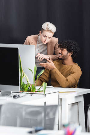 happy indian designer pointing at computer monitor near advertising managerの写真素材