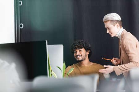 blonde woman pointing at computer monitor near indian advertising designerの写真素材