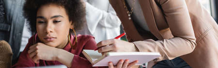 pensive african american woman thinking near colleague with notebook in ad agency, bannerの写真素材