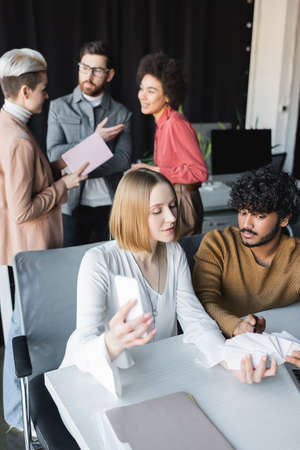 indian man pointing at samples near colleague and interracial team talking on blurred background