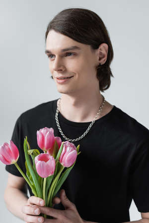 Smiling stylish man holding tulips isolated on grey